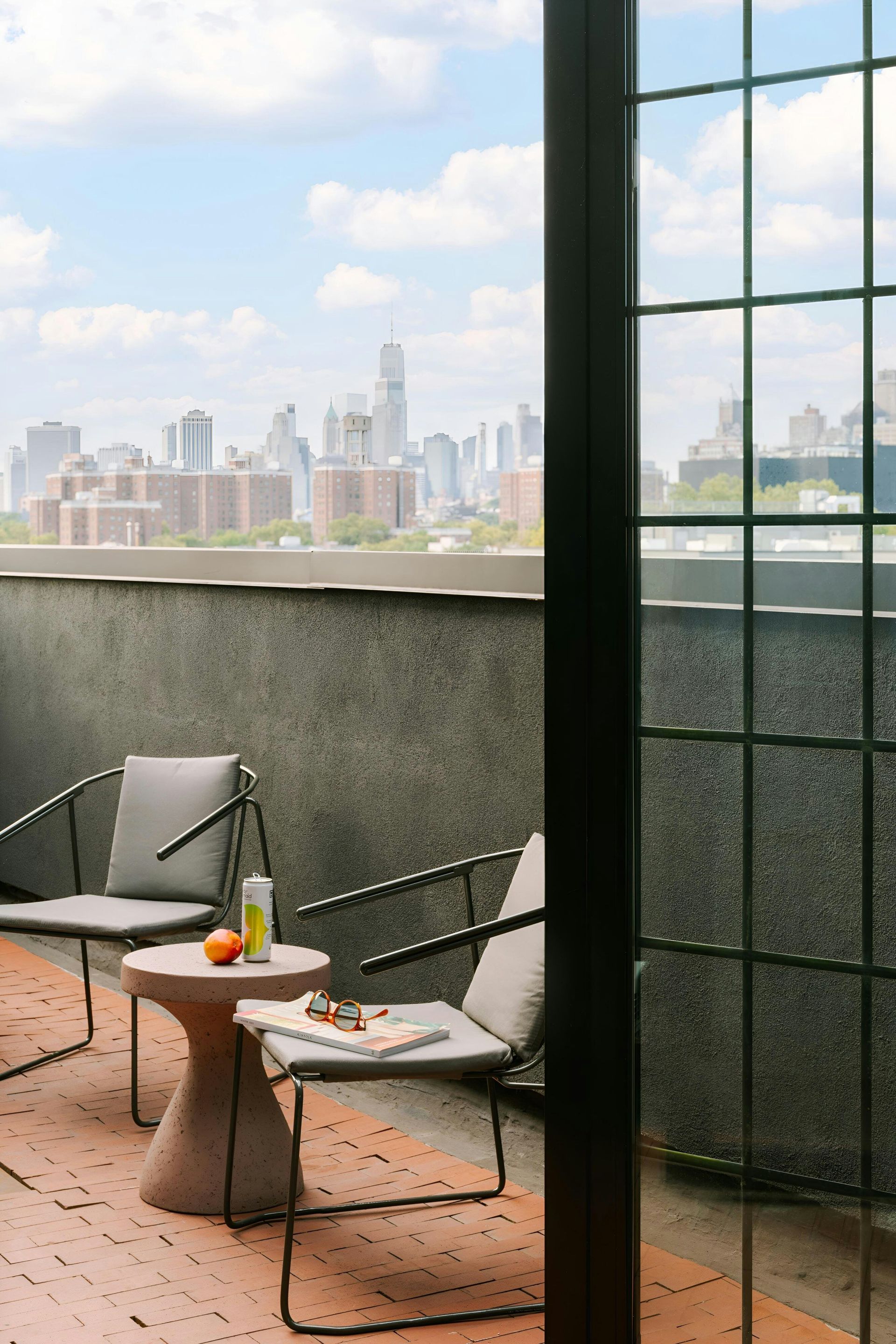 Two chairs and a small table on a balcony overlooking a city skyline under a blue sky.