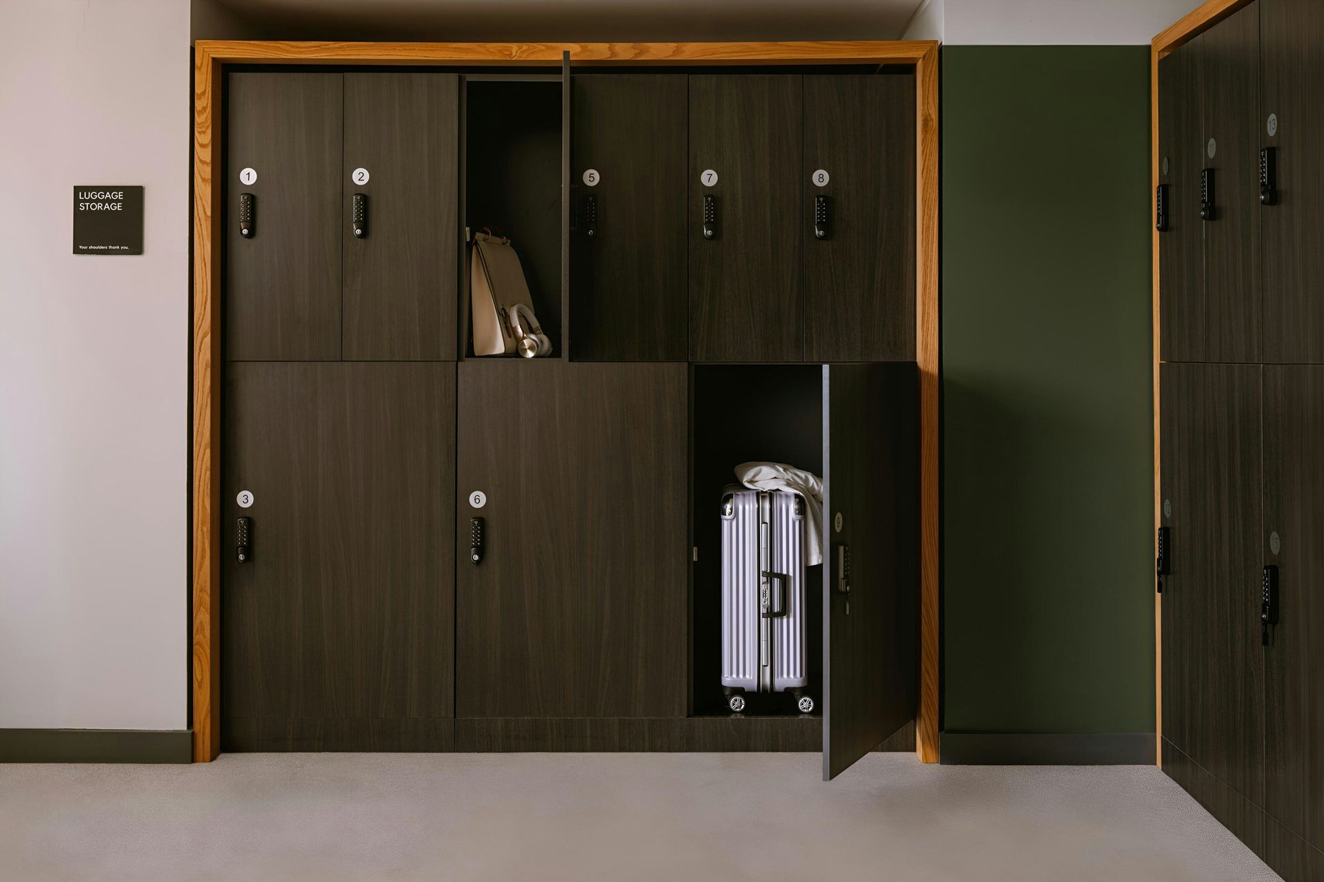 Dark wood lockers set against a white wall, with one open door revealing a silver suitcase inside.