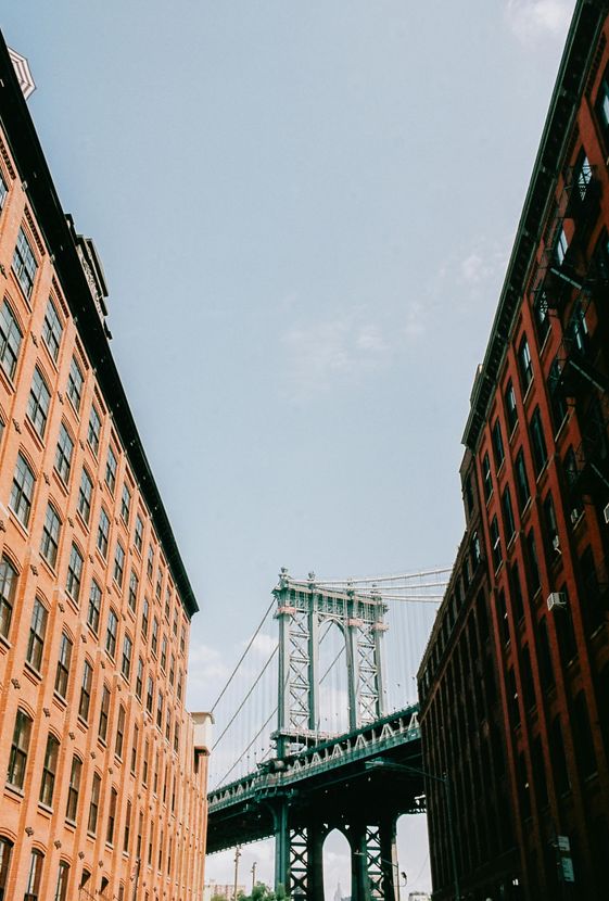 The Manhattan Bridge viewed from below between two tall, classic brick apartment buildings in New York City.