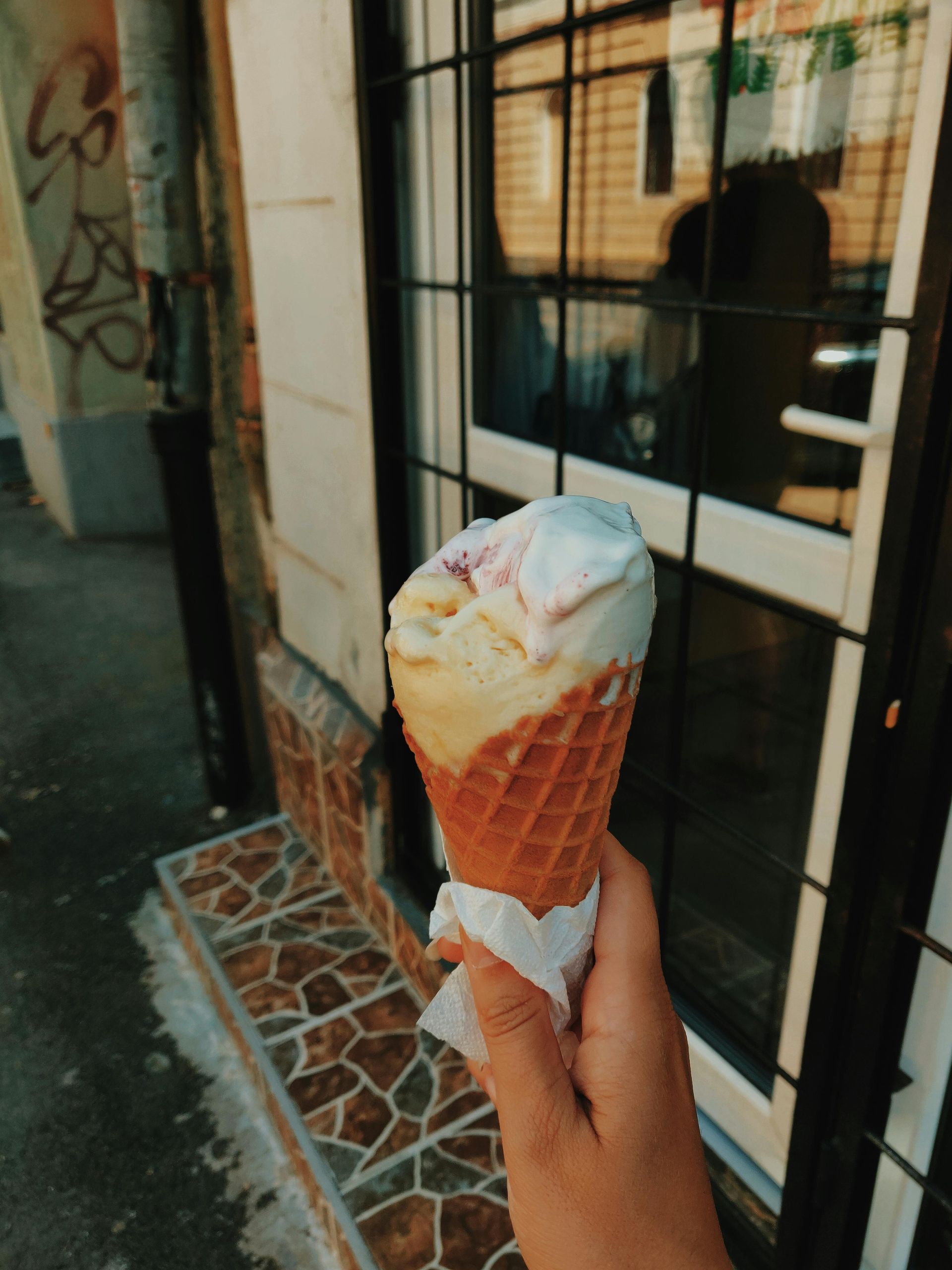 A hand holds a partially eaten, multi-colored ice cream cone against a building with a metal-grated door.