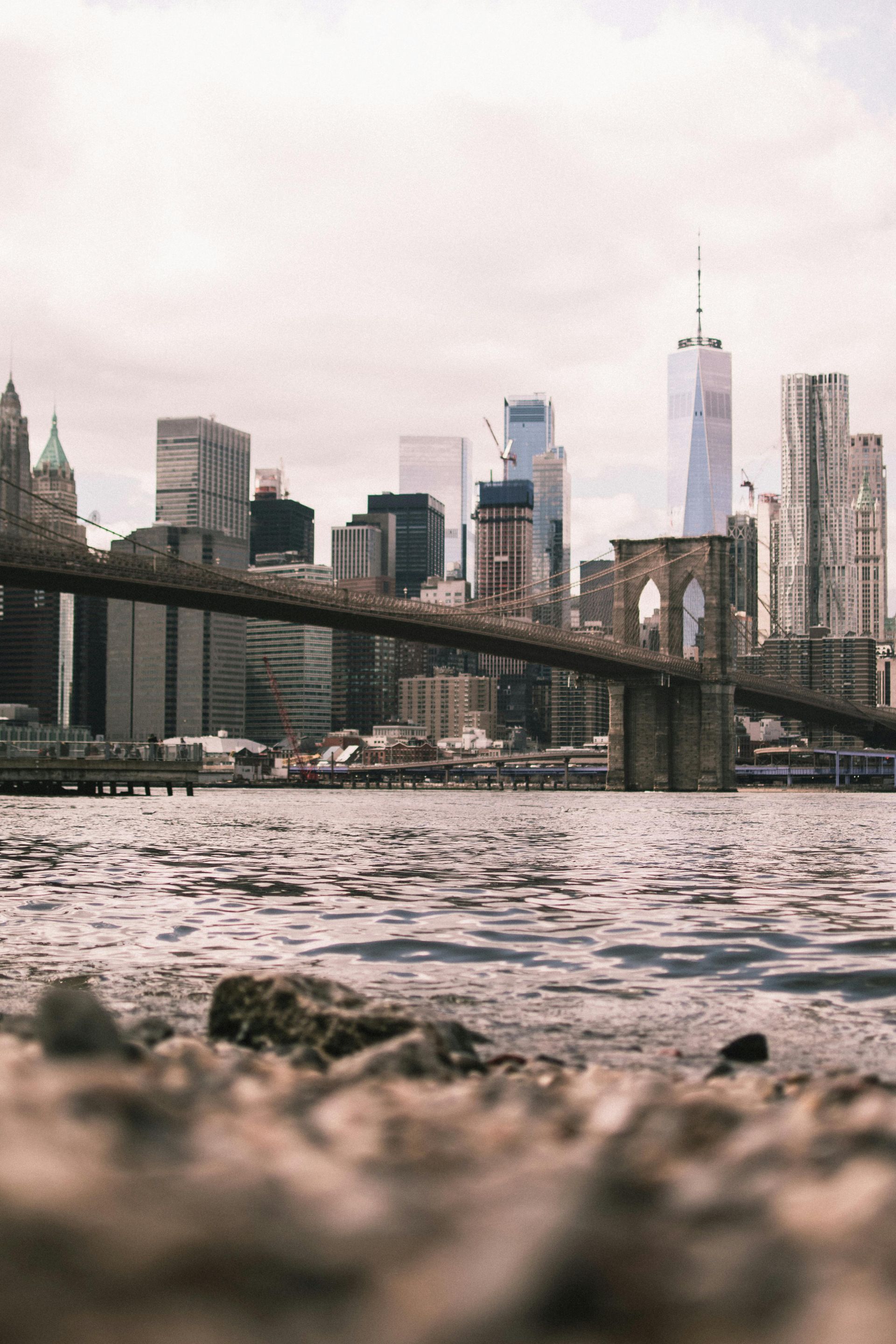 Low-angle view of the Brooklyn Bridge with the New York City skyline and One World Trade Center in the background.