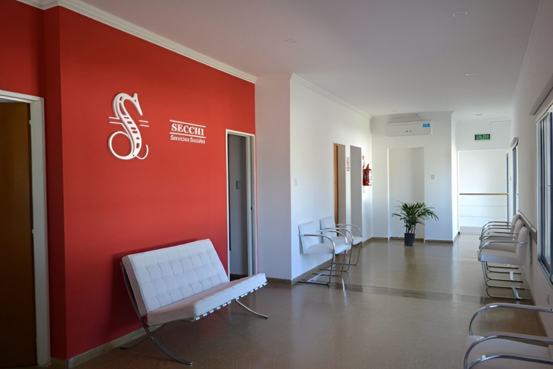 Una sala de espera con una pared decorativa roja que luce un logotipo, bancos modernos.