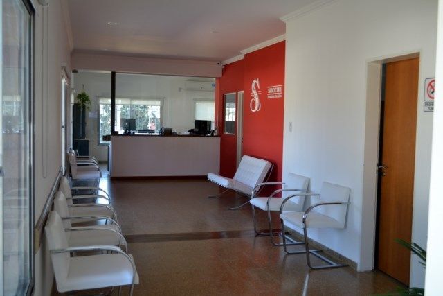 Una sala de espera luminosa y moderna con sillas blancas dispuestas en filas y una pared decorativa.