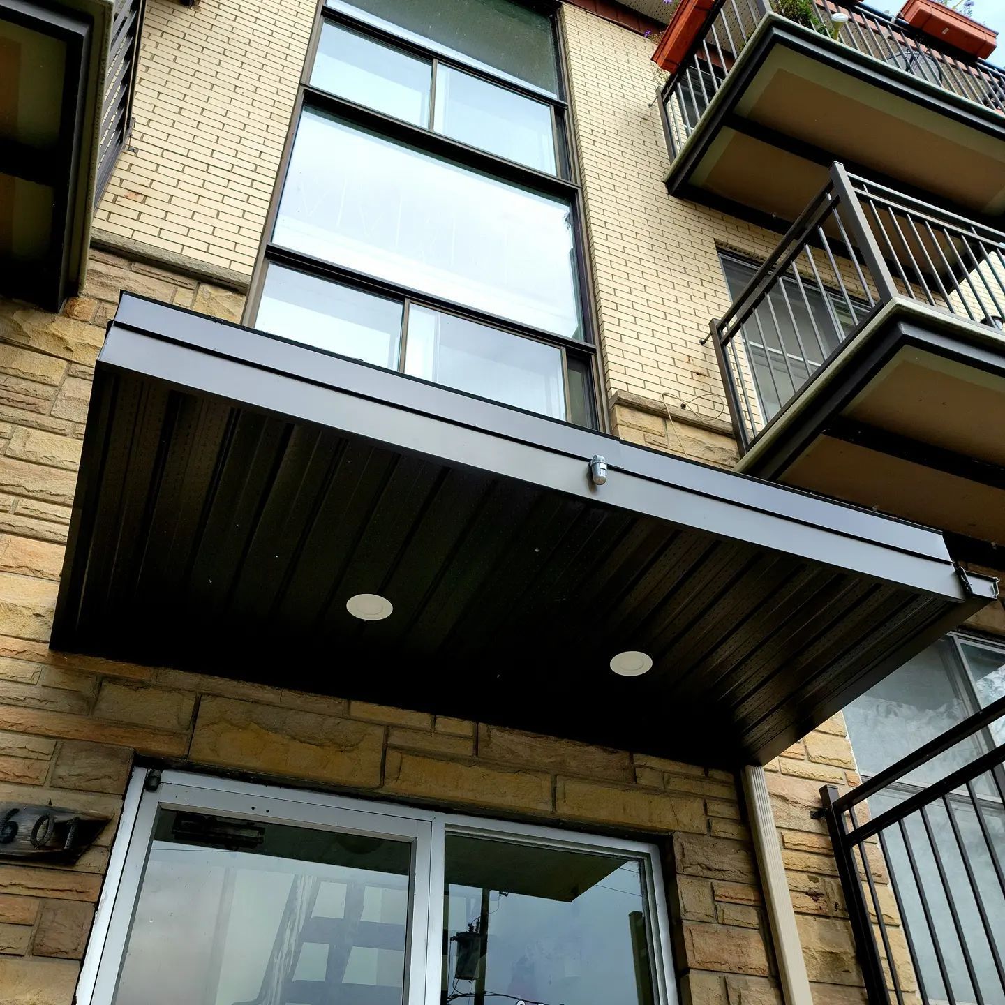 Extérieur du bâtiment avec balcons, auvent et grandes fenêtres; façade en briques beiges.