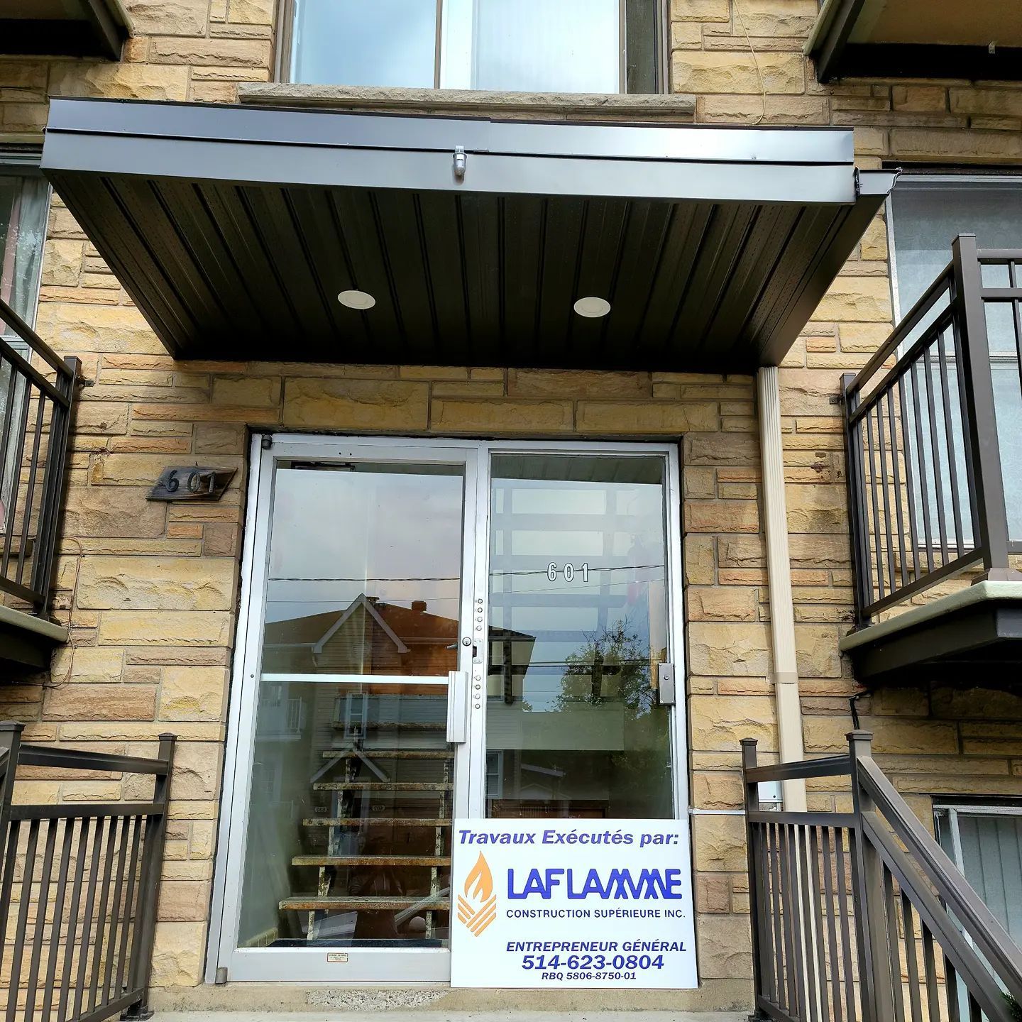 Entrée d'immeuble avec porte vitrée, escalier et pancarte Laflamme.