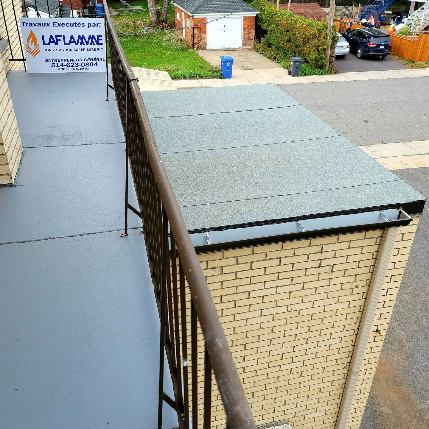 Un mur de briques avec un toit plat et une balustrade en métal, donnant sur une rue.