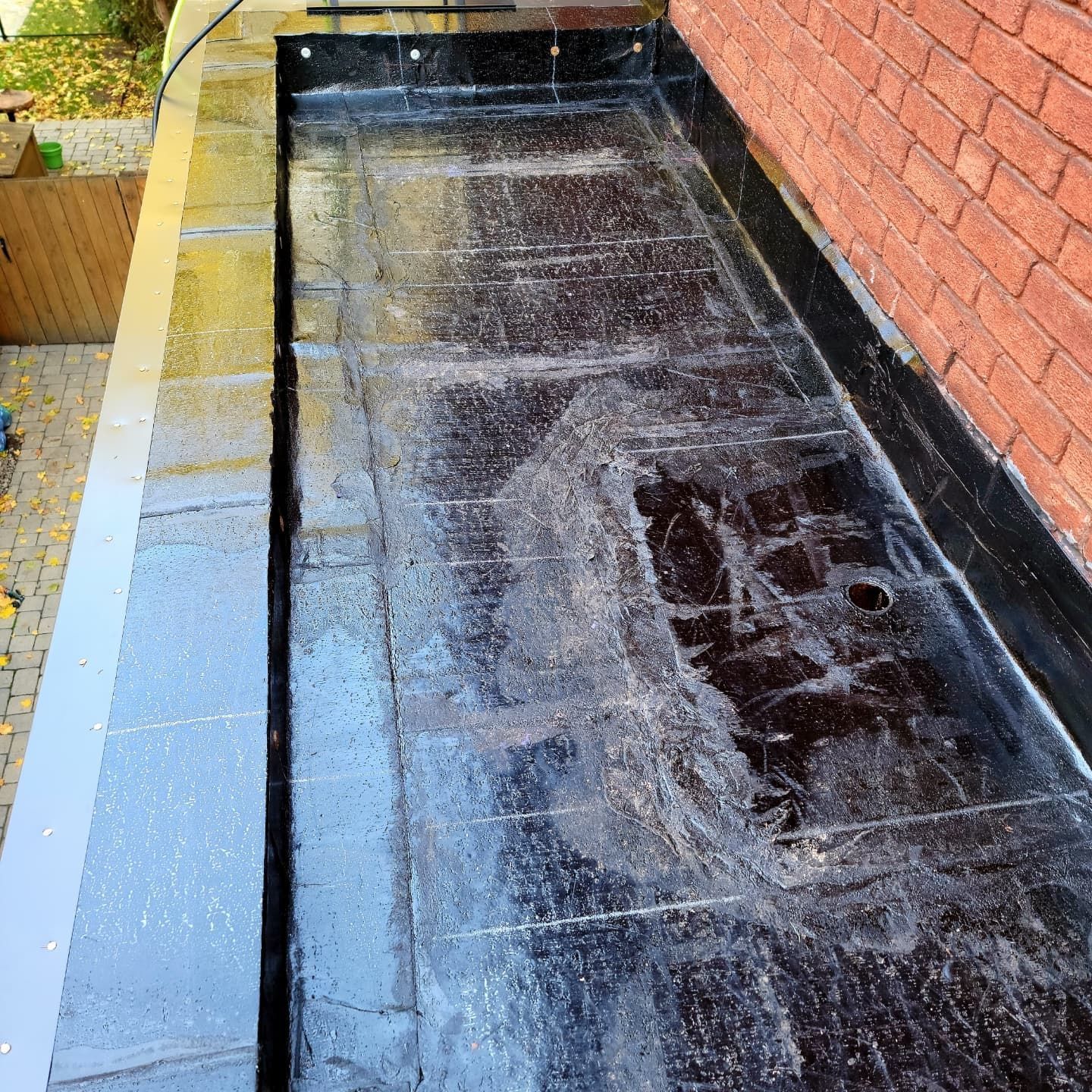 Bassin rectangulaire noir avec revêtement foncé, contre un mur de briques et un pavage.