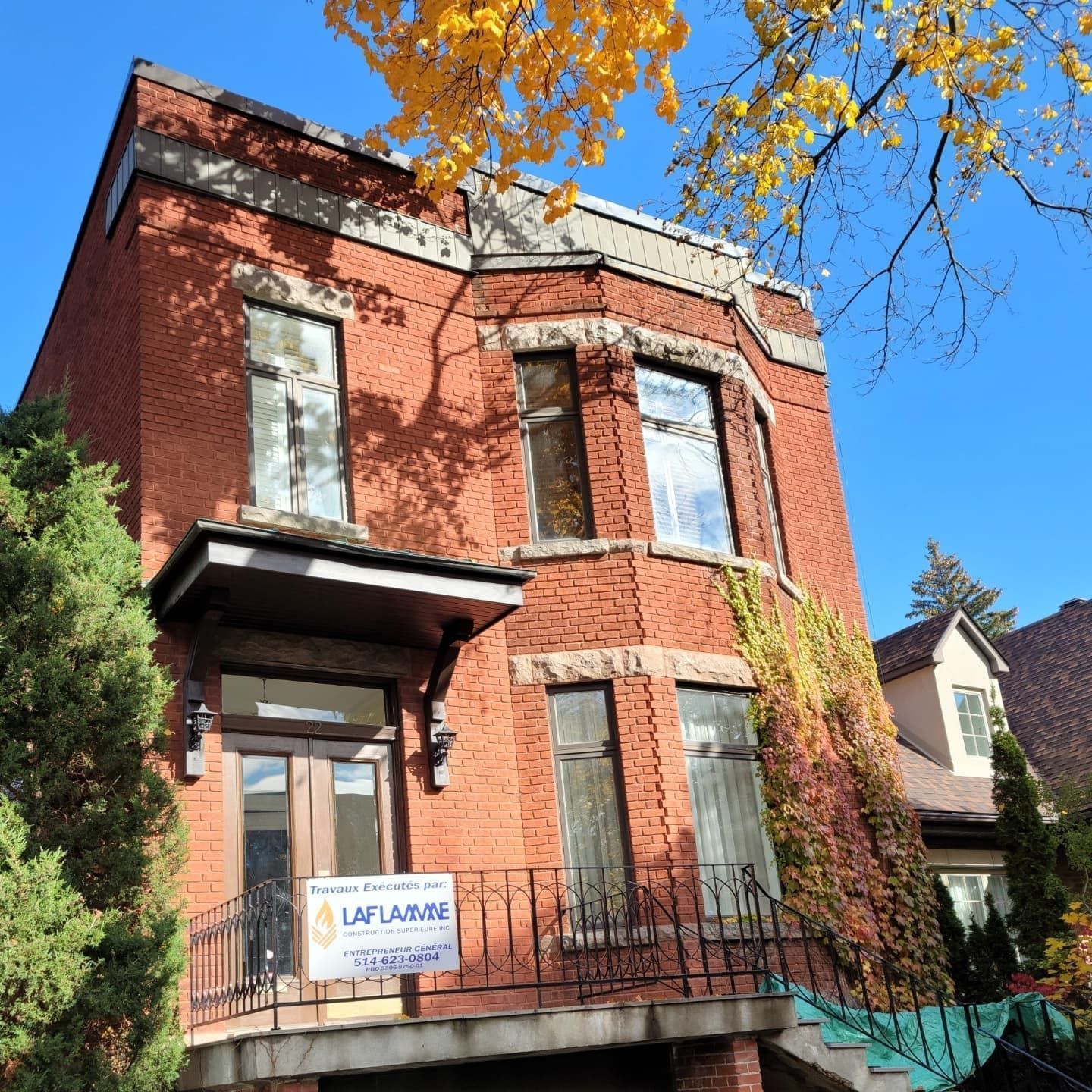 Bâtiment en briques rouges avec baie vitrée, marches et garde-corps en fer forgé. Enseigne : LAFLAMME. Feuilles d'automne.