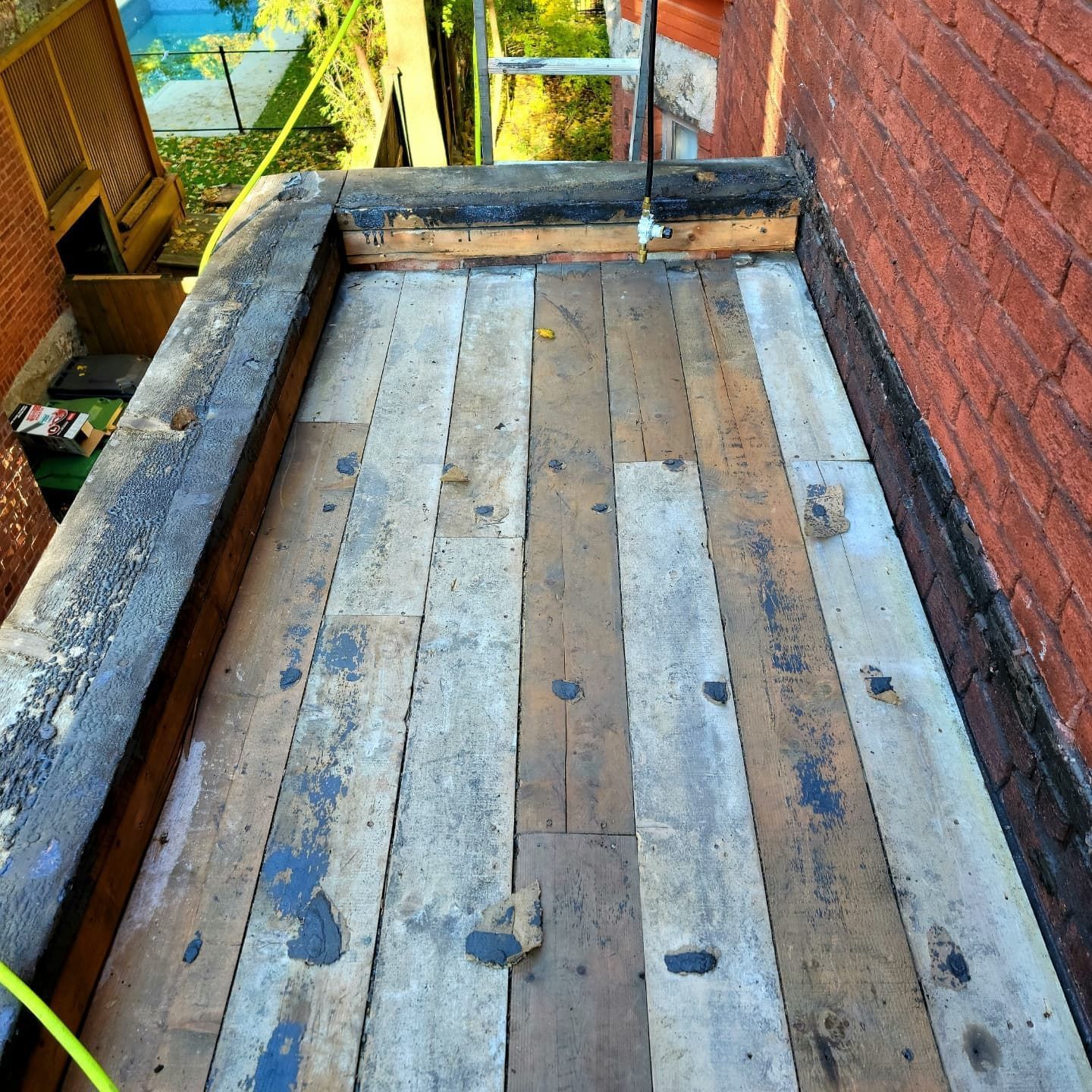 Toit en bois avec planches patinées, entouré d'un mur de briques et de boiseries.
