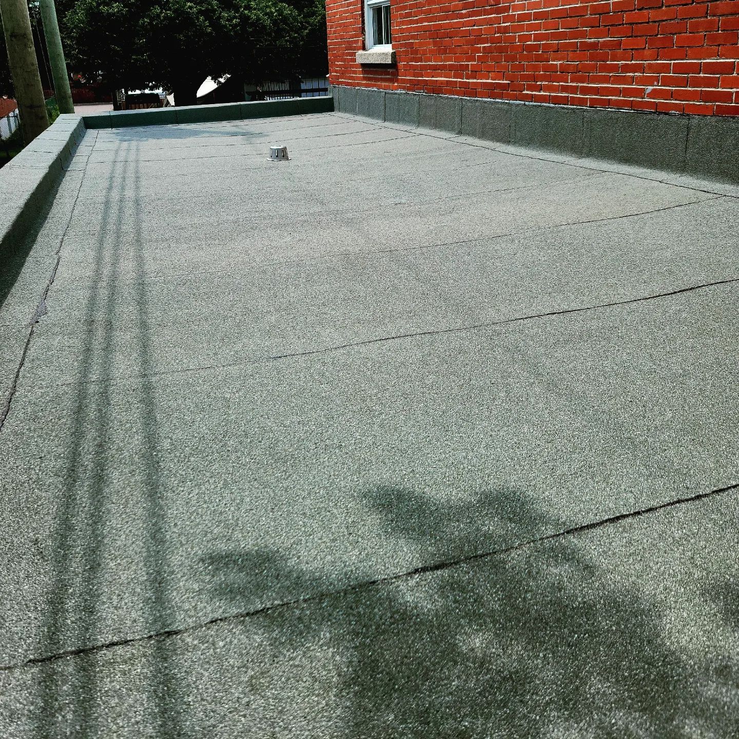 Toit plat gris foncé avec une surface texturée à côté d'un bâtiment en briques rouges par une journée ensoleillée.