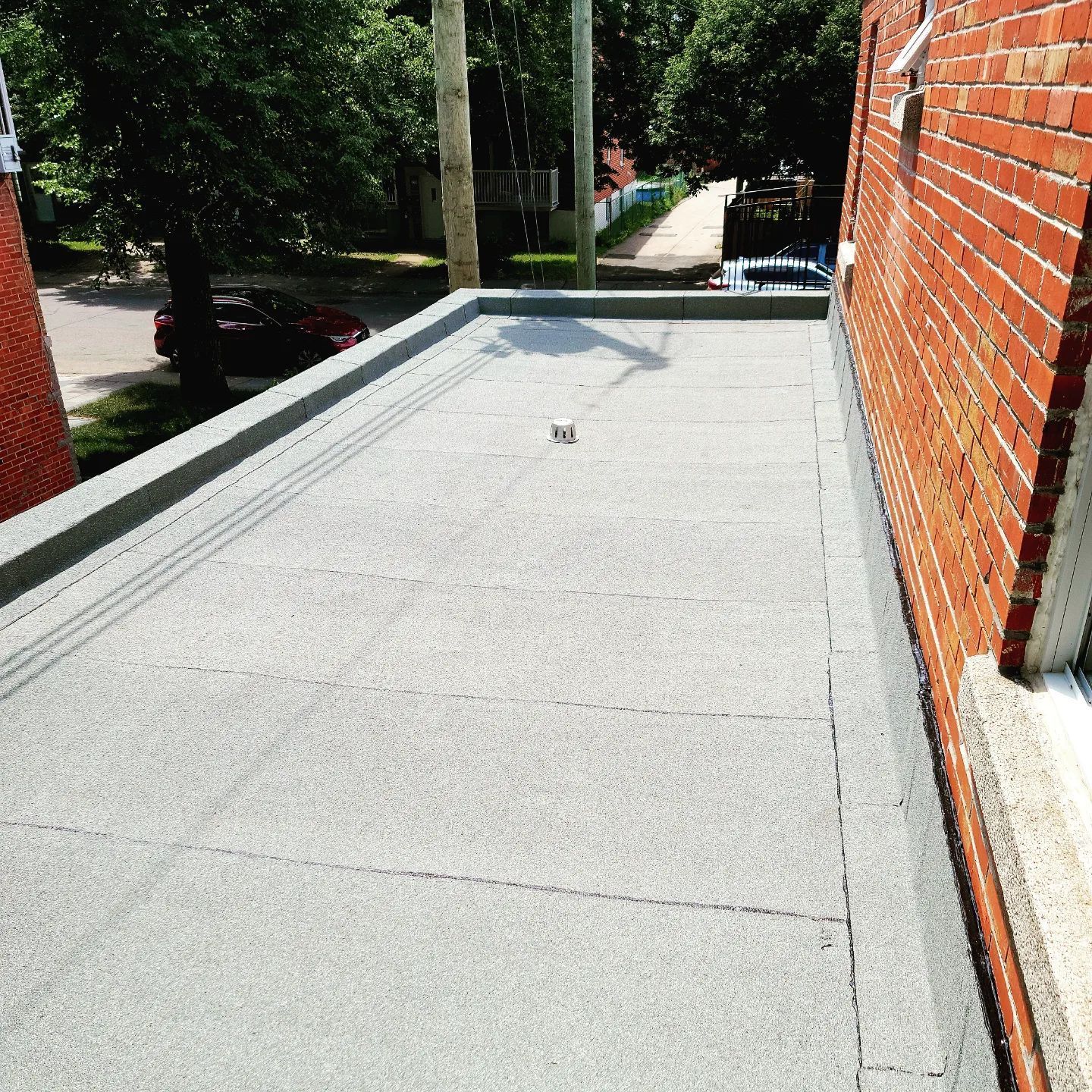 Toit plat, surface grise, adjacent à un bâtiment en briques. La lumière du soleil projette des ombres sur le toit.