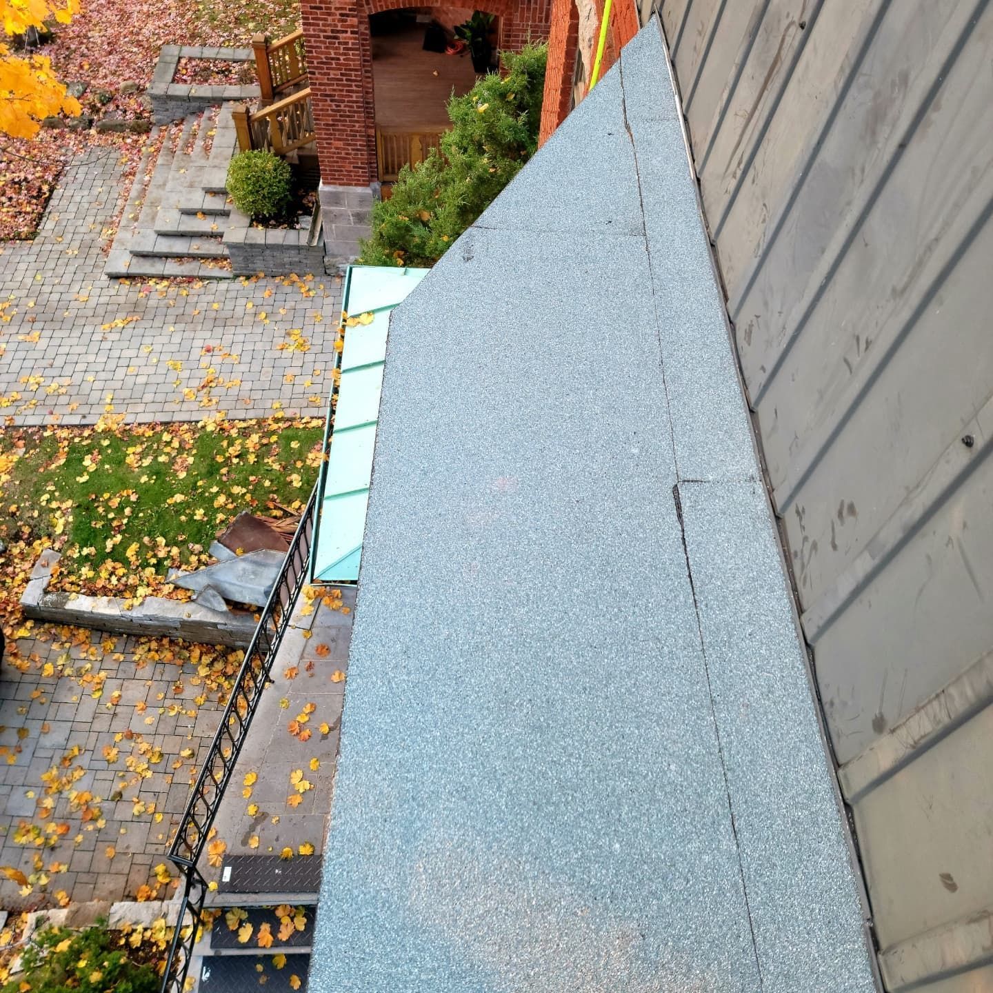 Vue depuis le toit d'un bâtiment avec un matériau de toiture gris, donnant sur un patio en pierre avec des feuilles d'automne.