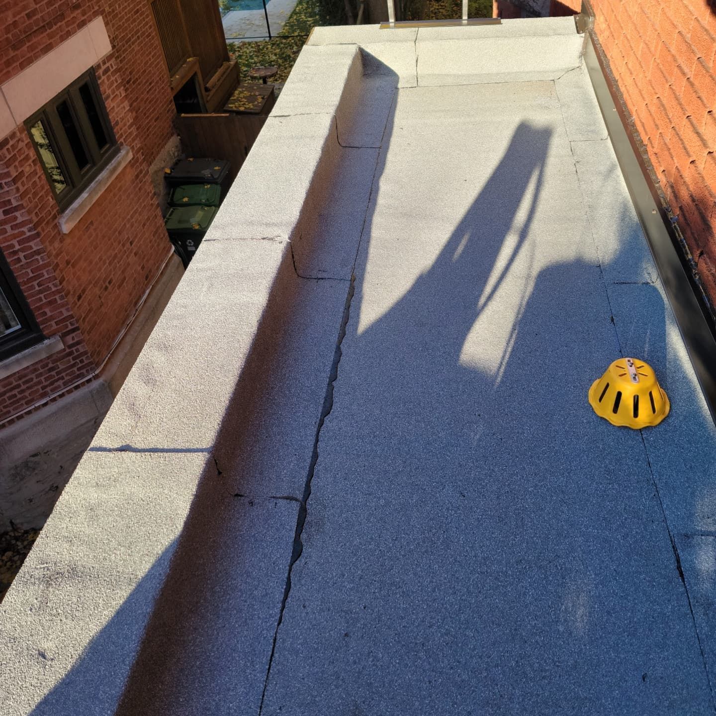 Toit plat avec couvercle de drain jaune, ombres et fissures. Extérieur du bâtiment de chaque côté.