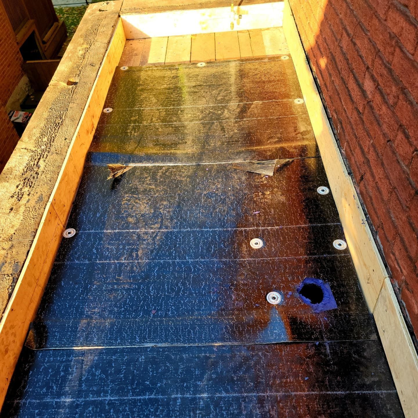 Membrane imperméable foncée sur une ossature en bois, probablement pour un toit ou une terrasse, avec quelques attaches et une zone bleue.