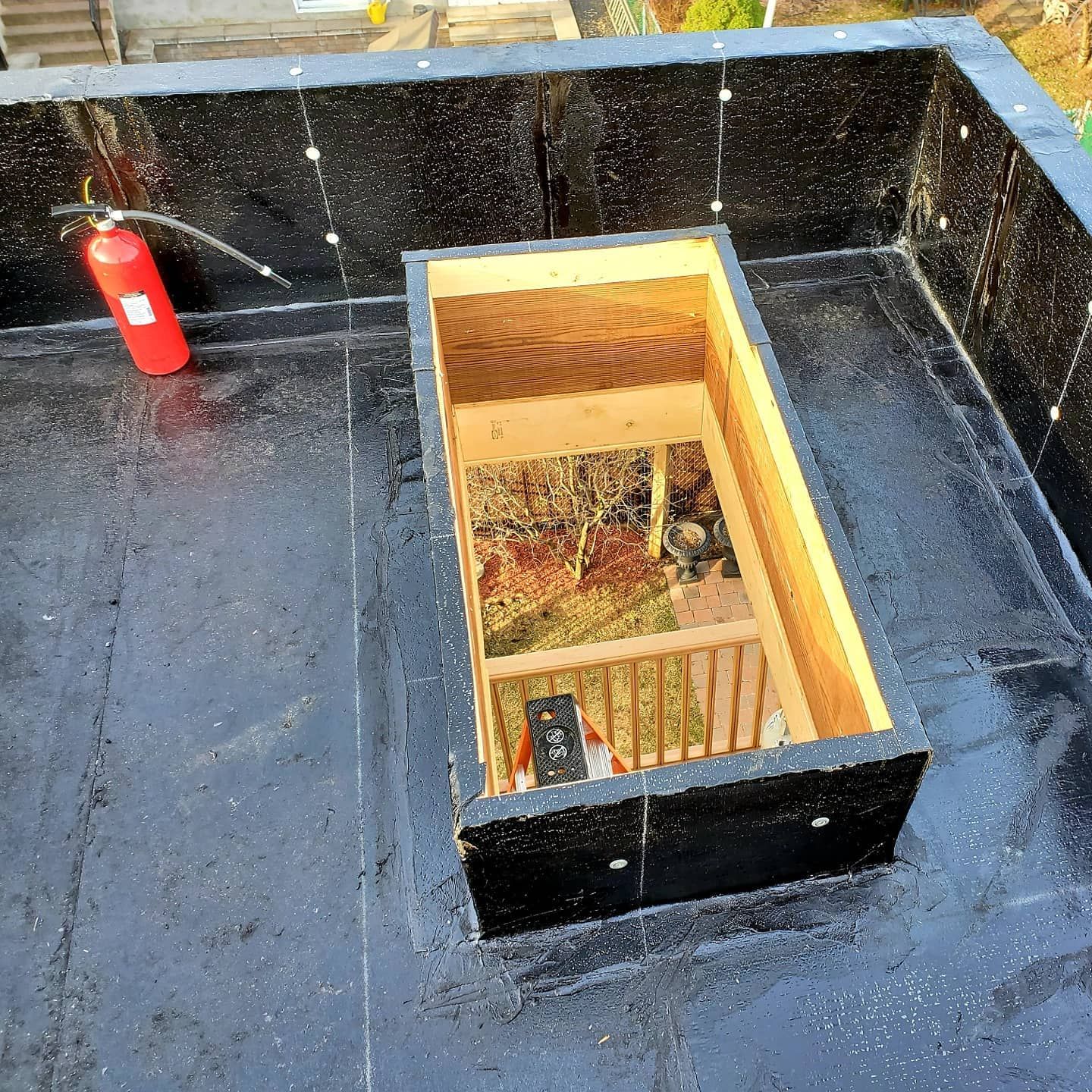 Vue du toit d'une lucarne rectangulaire en bois avec un extincteur à côté. Toiture et boiseries noires.