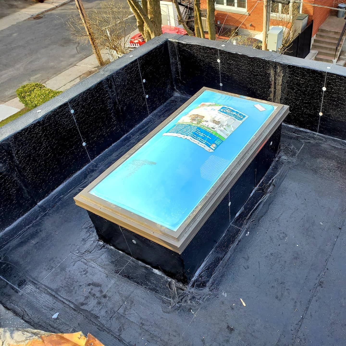 Une lucarne sur un toit plat en goudron noir. Le verre bleu est encadré de brun.