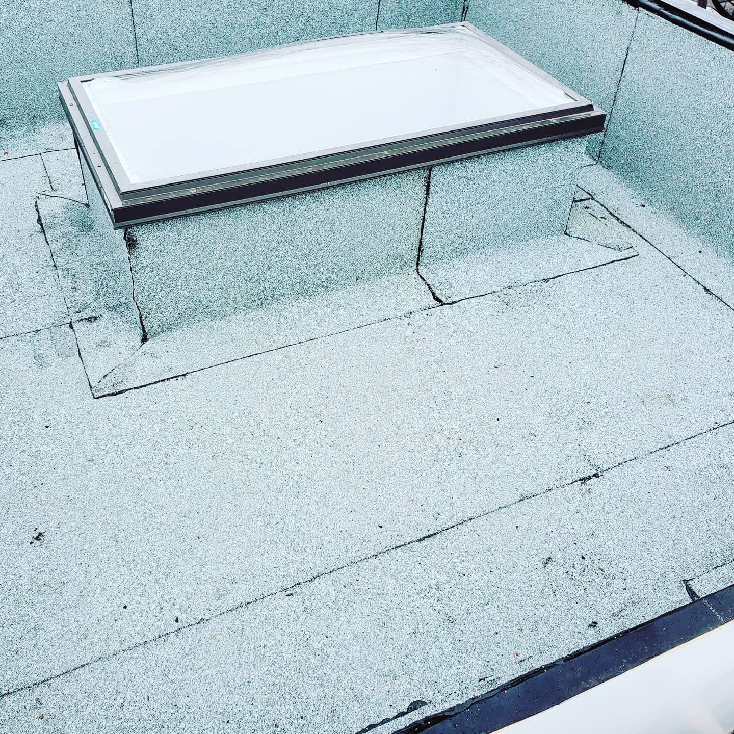 Puits de lumière sur un toit plat recouvert de granulats. Bordure foncée autour de la fenêtre et bordures foncées autour du toit.