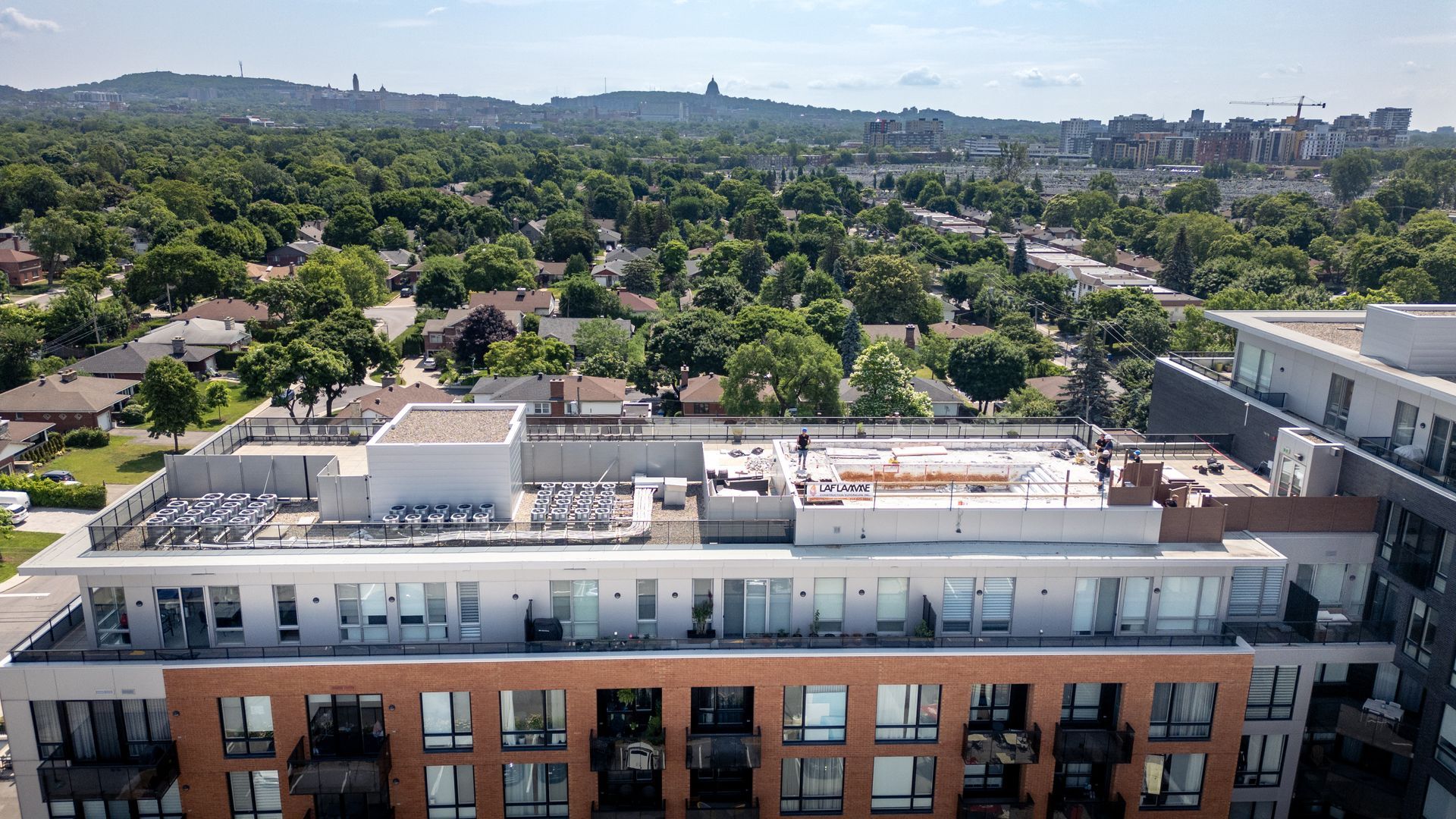 Vue aérienne d'un immeuble d'appartements avec des commodités sur le toit, des arbres et la ligne d'horizon lointaine de la ville.
