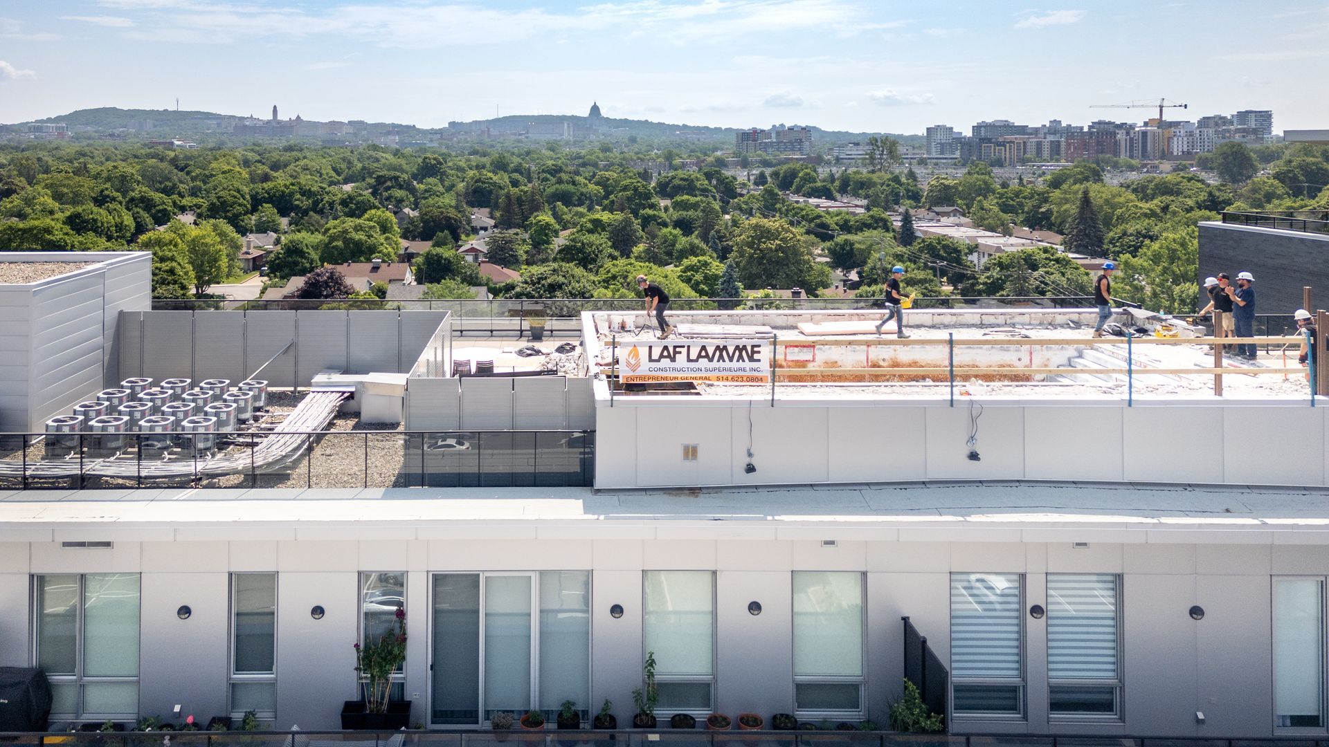 Des ouvriers du bâtiment sur un toit avec une banderole sur laquelle on peut lire « LA LASALLE » ; journée ensoleillée, cadre urbain.