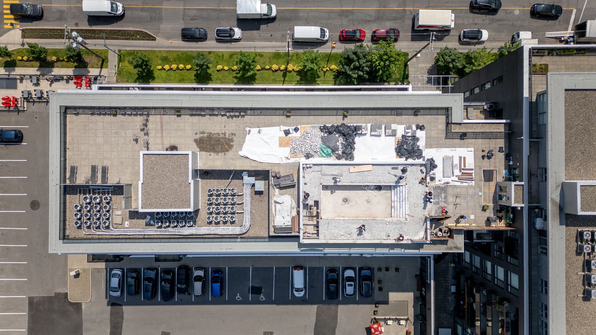 Vue aérienne du toit plat d'un bâtiment avec des débris et de l'équipement, surplombant une rue avec circulation et un parking.