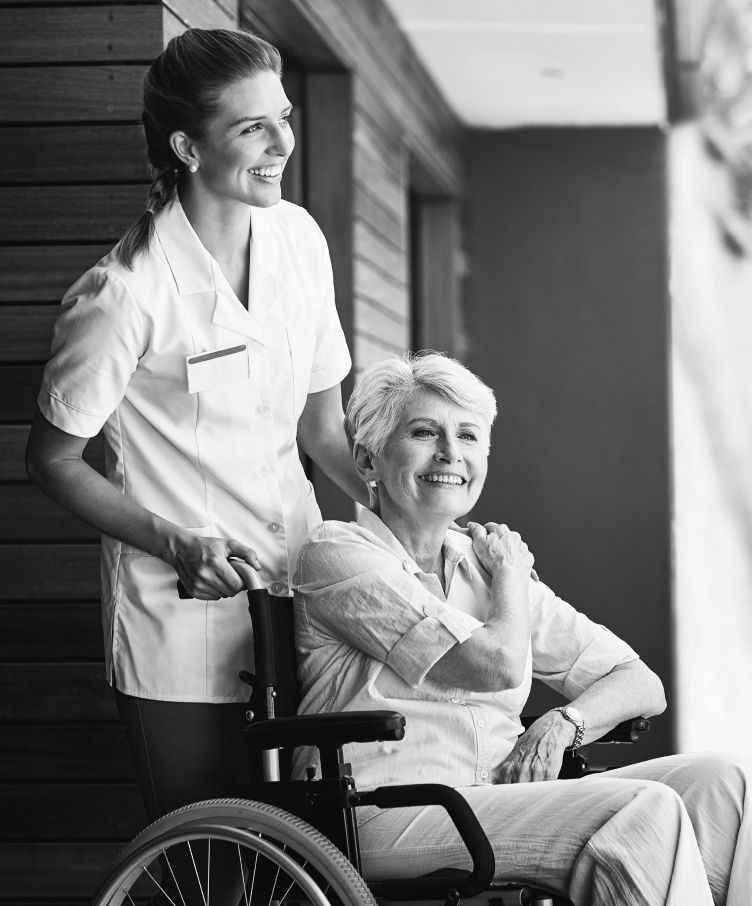A nurse is standing next to an elderly woman in a wheelchair.