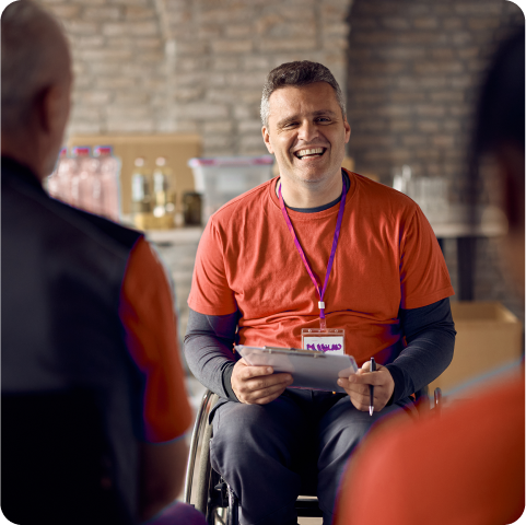 A man in a wheelchair is smiling while holding a clipboard.