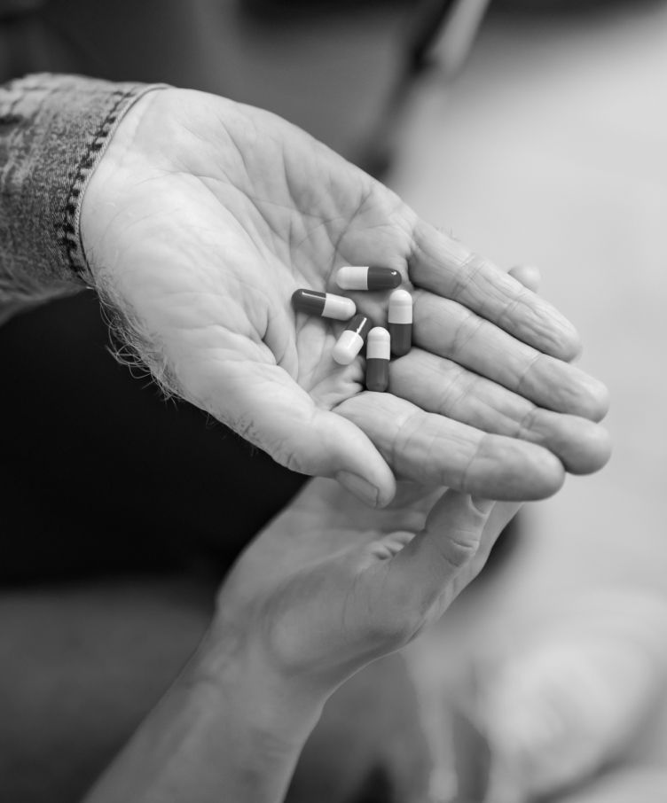 A person is holding a handful of pills in their hand.