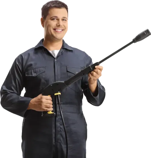 Man in blue jumpsuit holding a pressure washer, smiling.