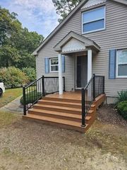 Front view of a house entrance with newly installed brown composite stairs, black metal railings, and a small porch roof.