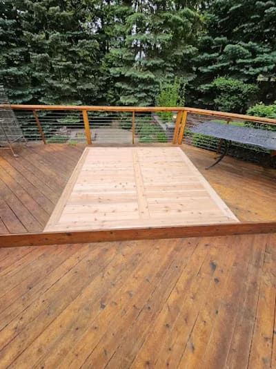 A wooden deck with a newly replaced, lighter-colored rectangular section in the center, surrounded by older, dark wood.