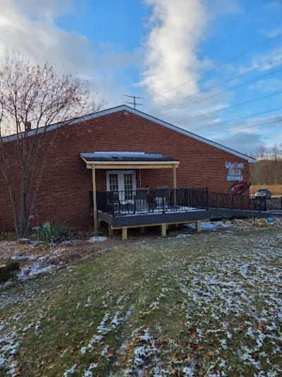 A brick building with a new wooden deck and dark metal railing under a roof overhang, set on a snowy, grassy lawn.