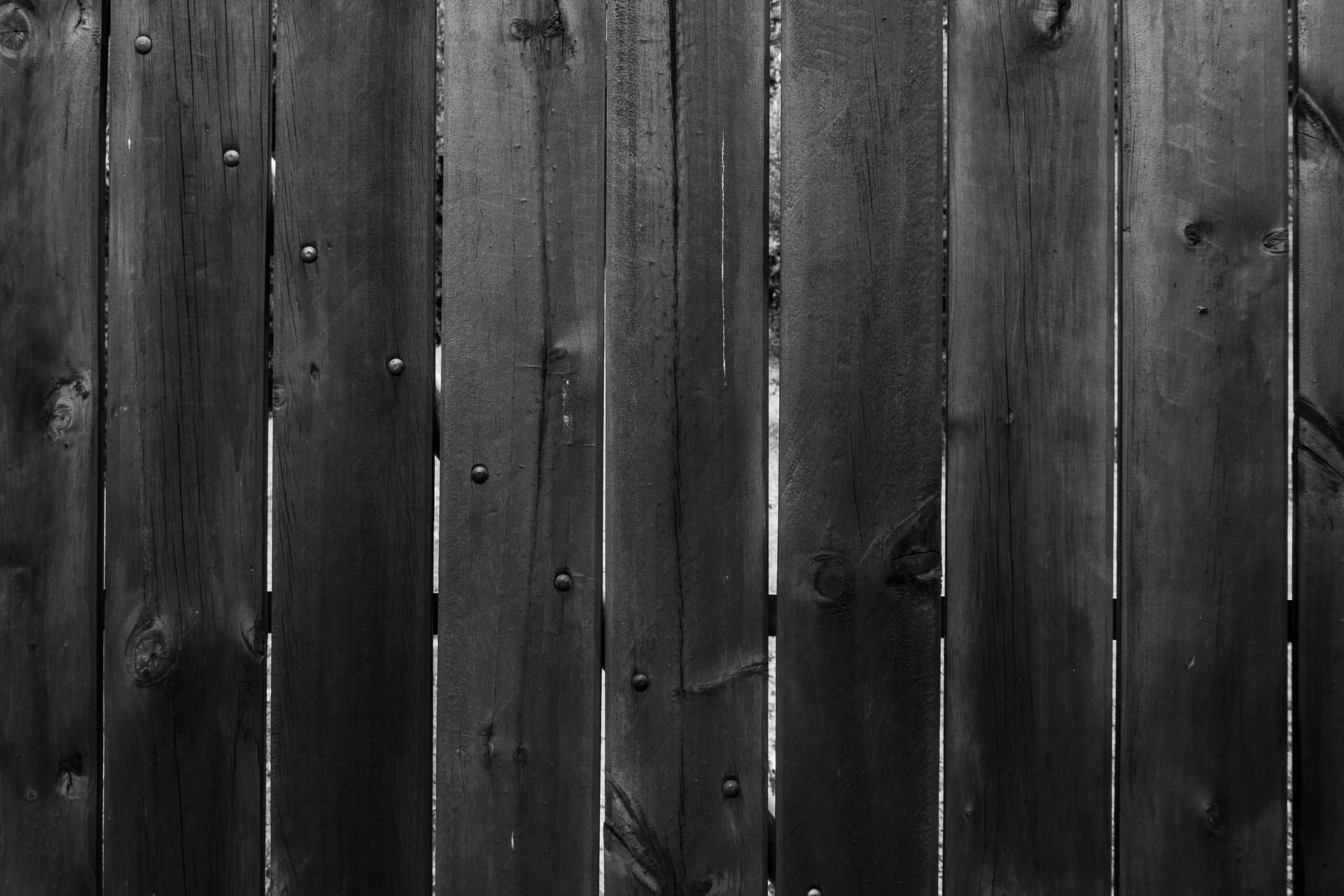 A close-up view of a dark, weathered wooden fence with vertical planks and visible wood grain.