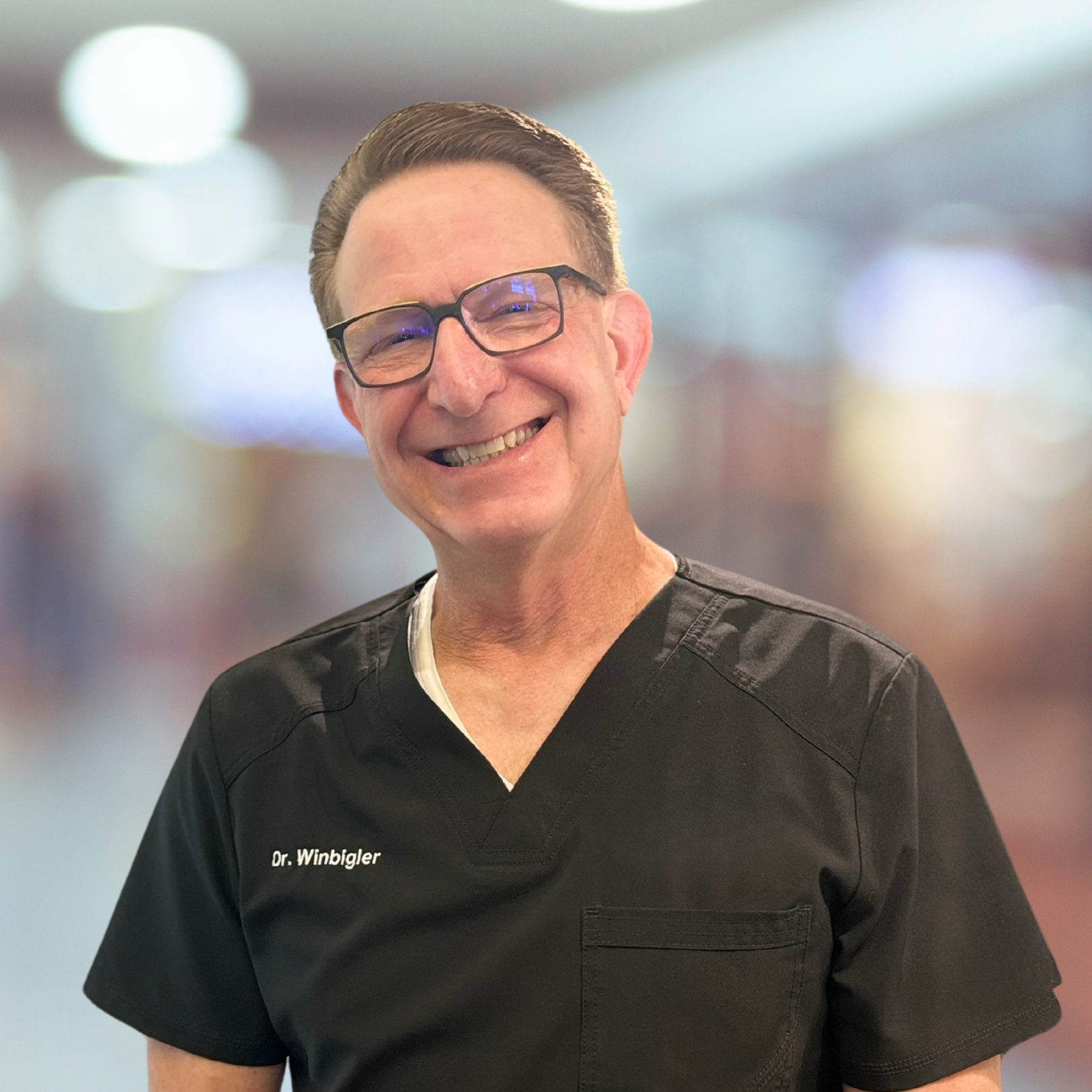 A man wearing scrubs and glasses is smiling for the camera