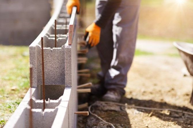 Worker laying concrete blocks on a foundation wall outdoors