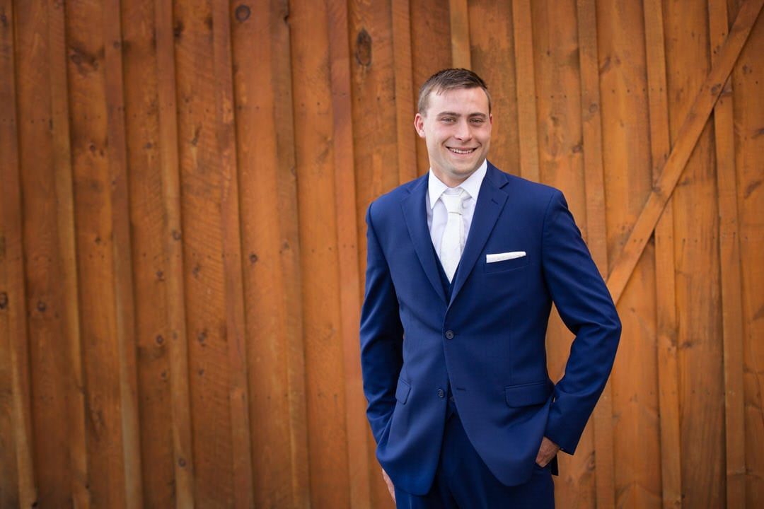 A man in a blue suit and tie is standing in front of a wooden wall.