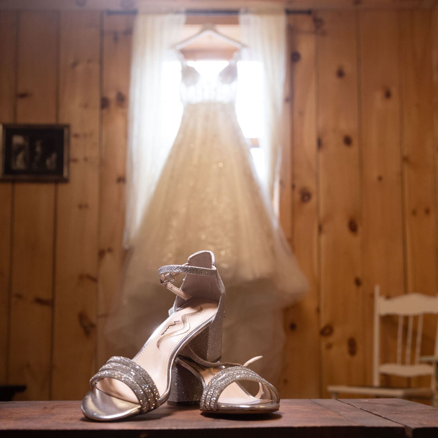 A pair of wedding shoes sit on a table in front of a wedding dress