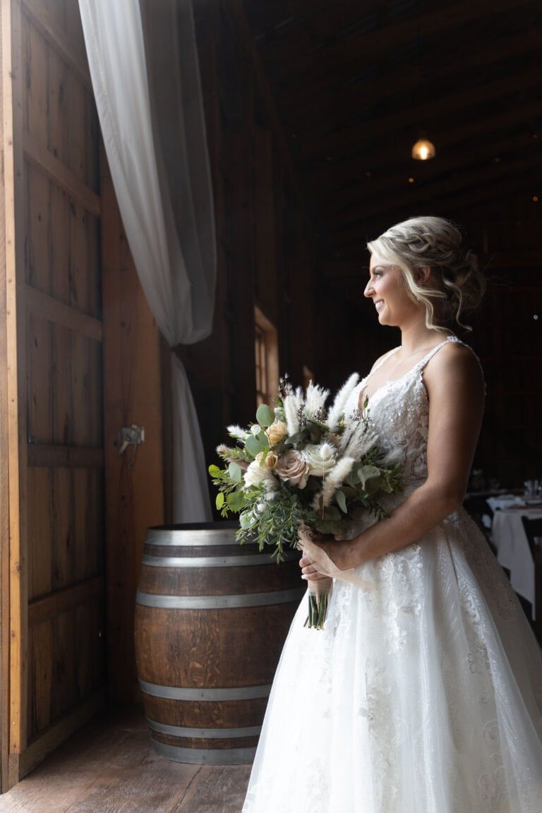 A bride in a wedding dress is standing in front of a window holding a bouquet of flowers.
