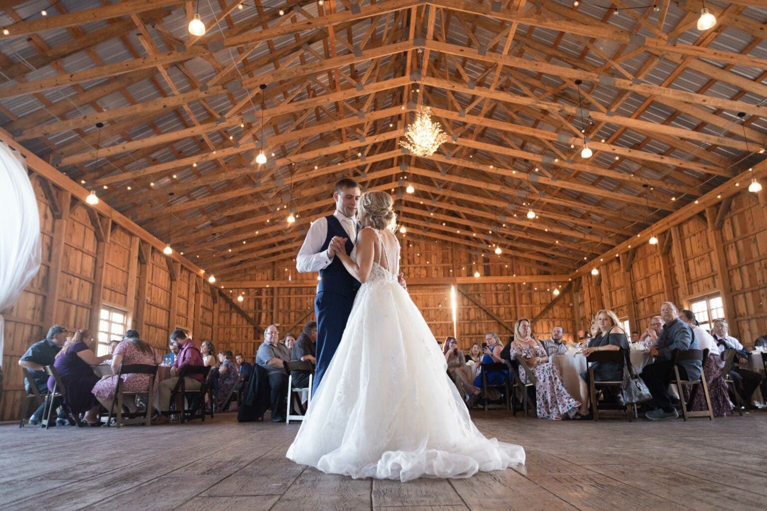 A bride and groom are dancing in a barn at their wedding reception.