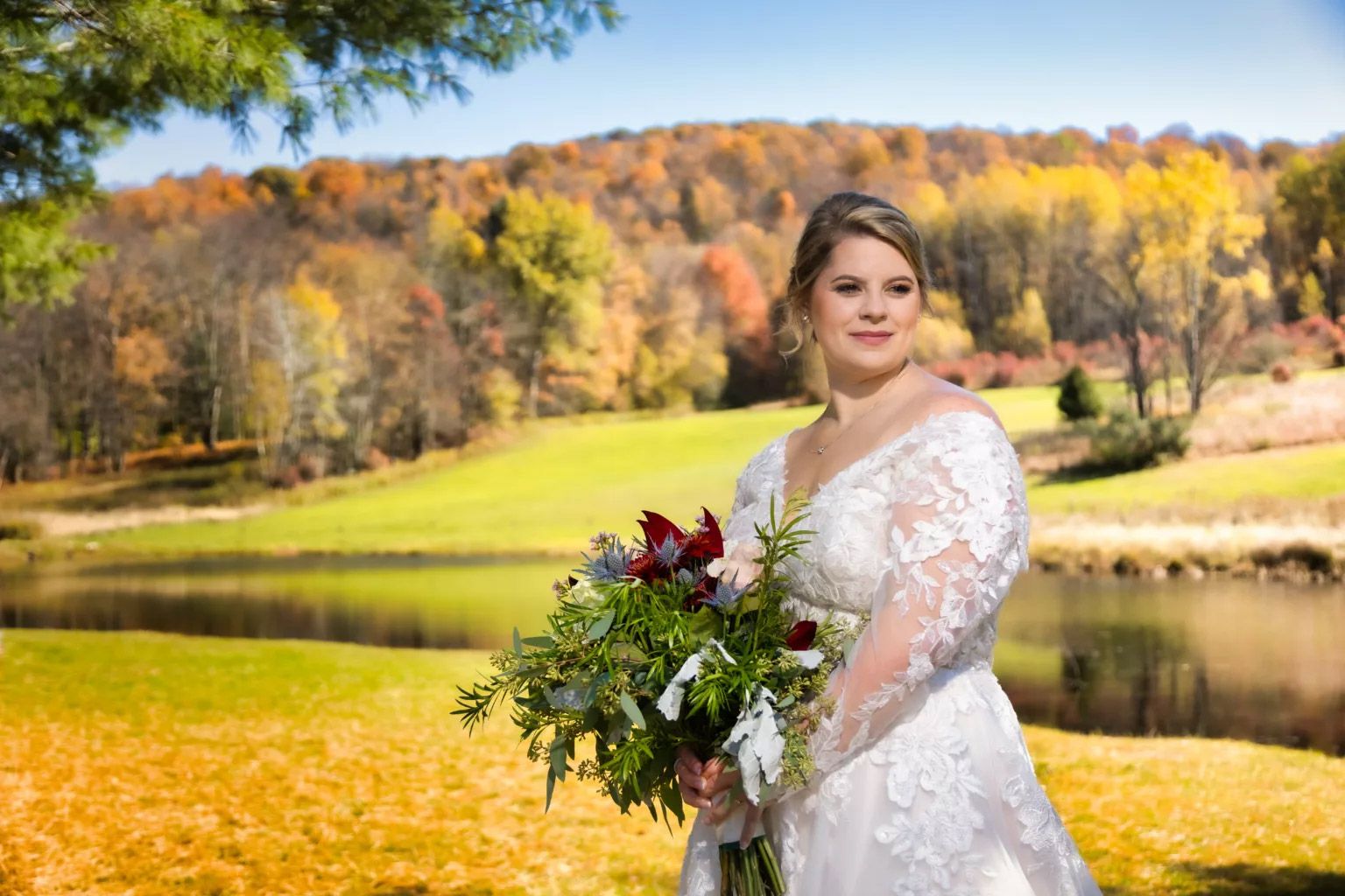 A bride in a wedding dress is holding a bouquet of flowers in front of a lake.