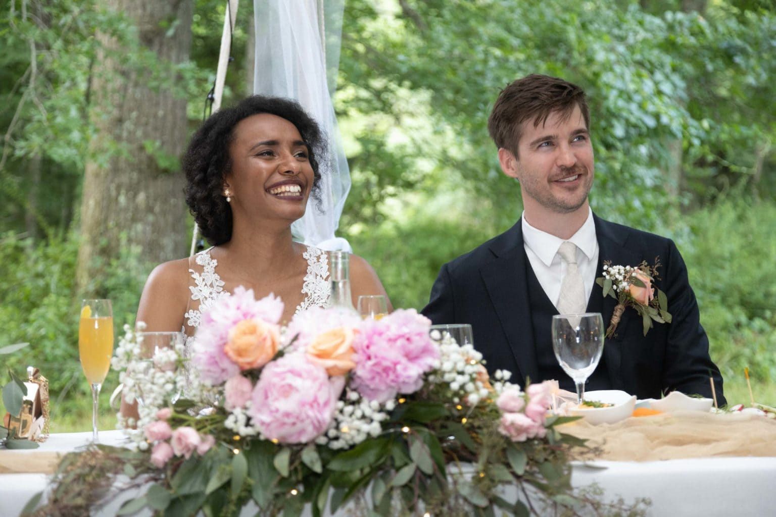 A bride and groom are sitting at a table with flowers and wine glasses.