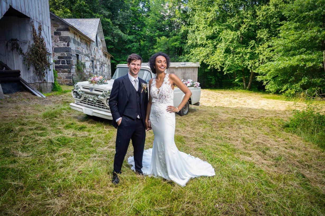 A bride and groom are posing for a picture in front of an old truck.