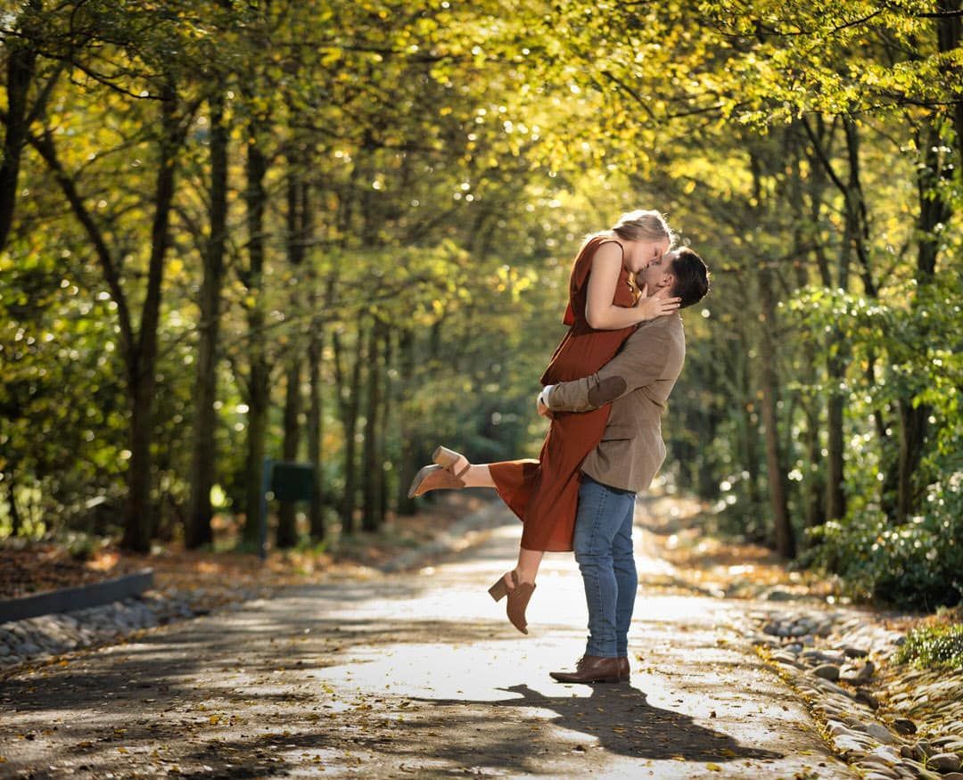 A man is holding a woman in his arms and kissing her in the woods.