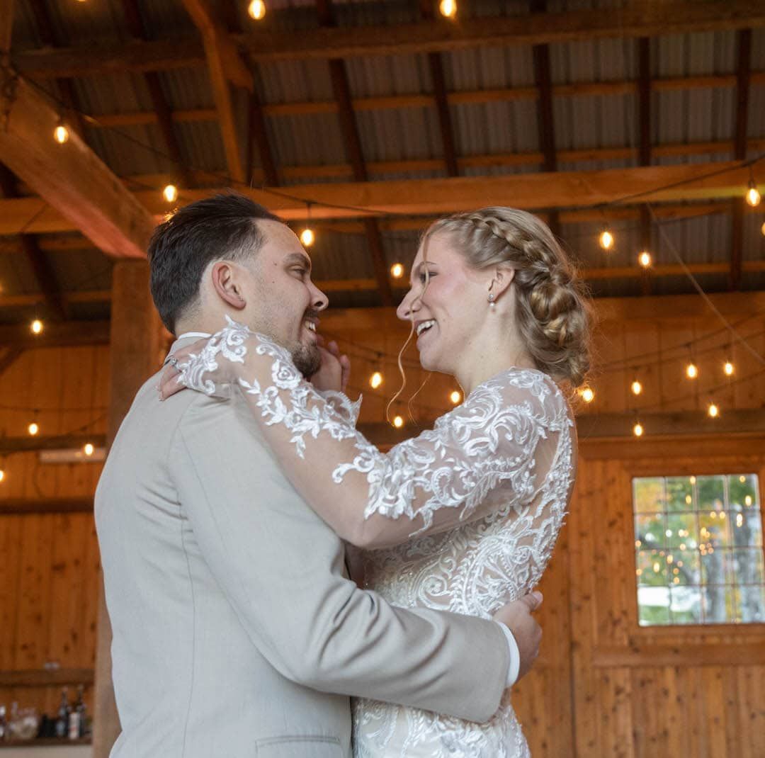 A bride and groom are dancing together in a barn.