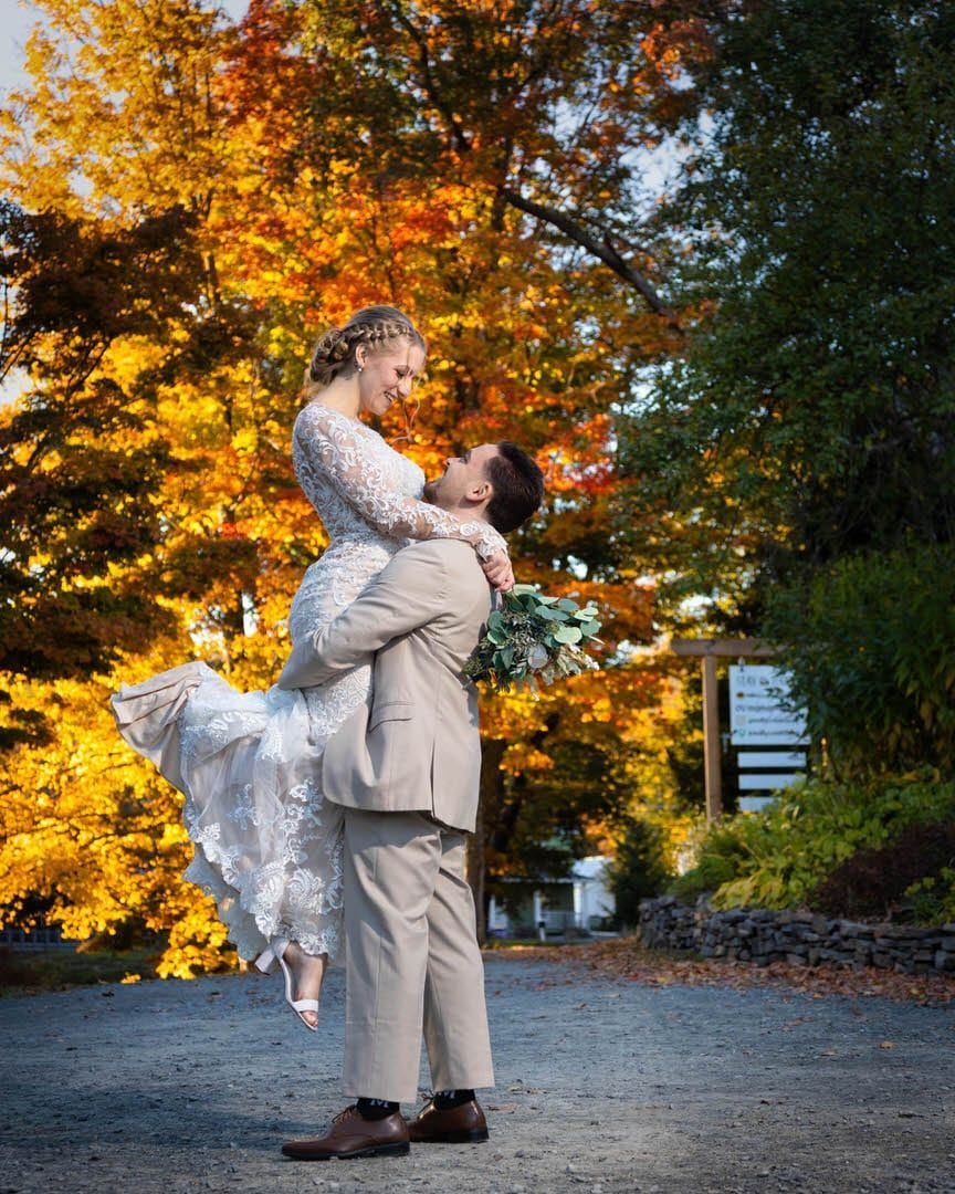 A bride and groom are posing for a picture in front of a tree with yellow leaves.