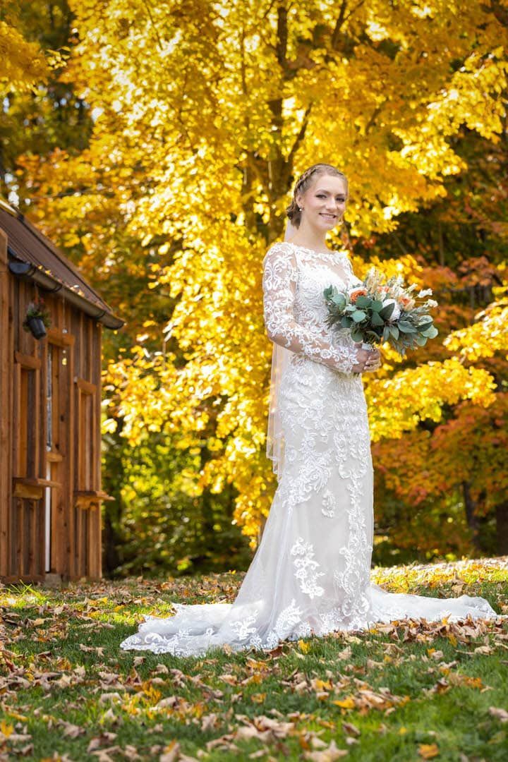 A bride in a wedding dress is standing in front of a shed holding a bouquet of flowers.