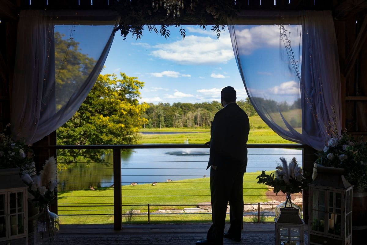 A man is standing on a balcony overlooking a lake.