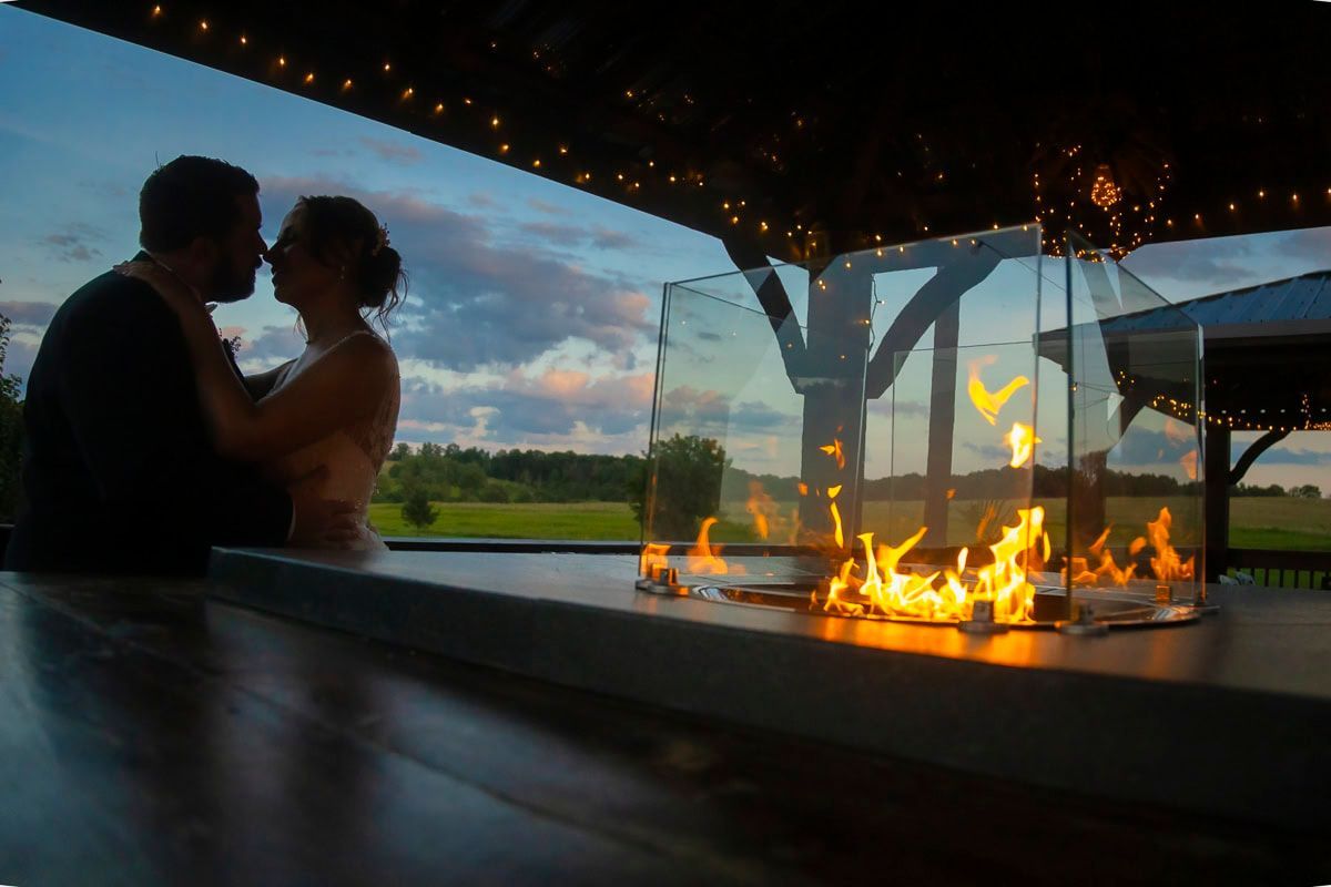 A bride and groom are kissing in front of a fire pit.
