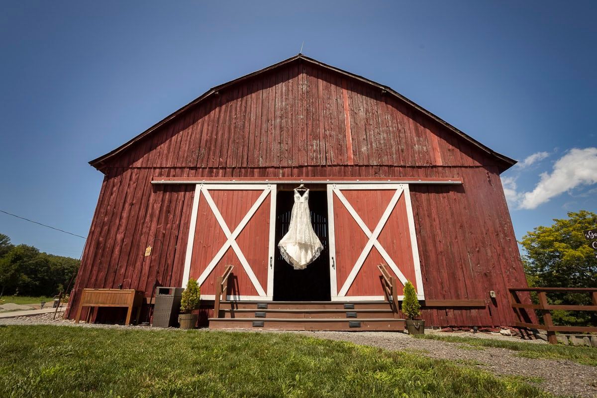 A bride in a wedding dress is standing in front of a red barn.
