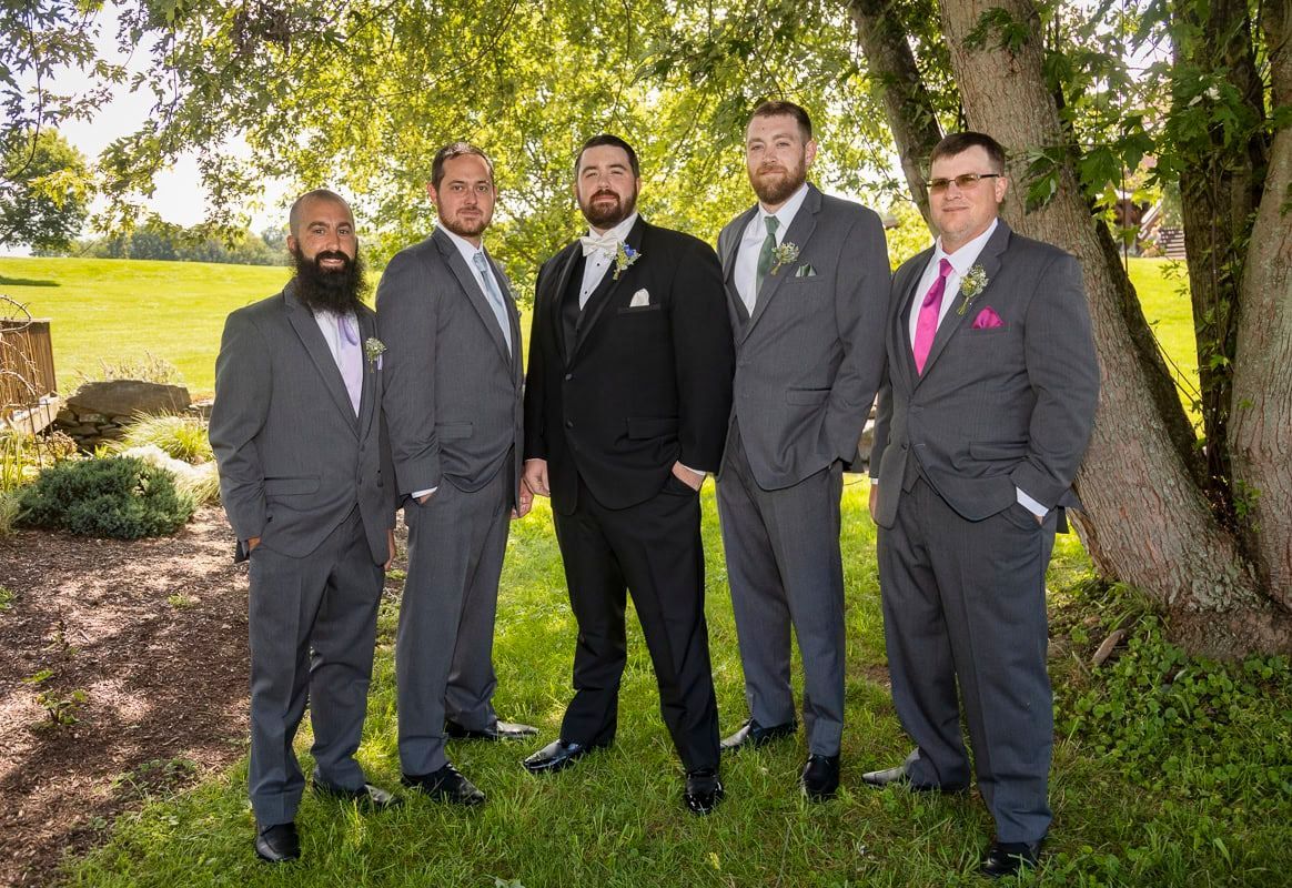 The groom and his groomsmen are posing for a picture in front of a tree.
