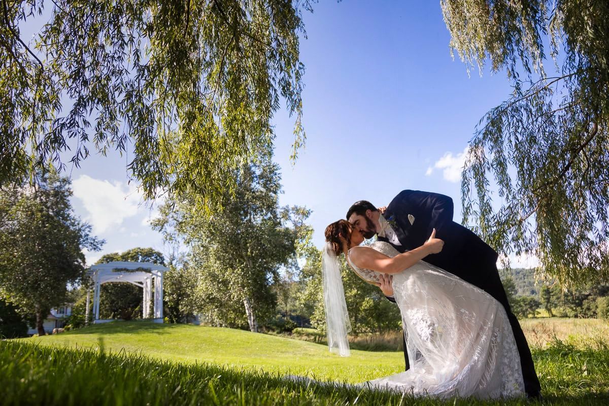A bride and groom are kissing under a willow tree.